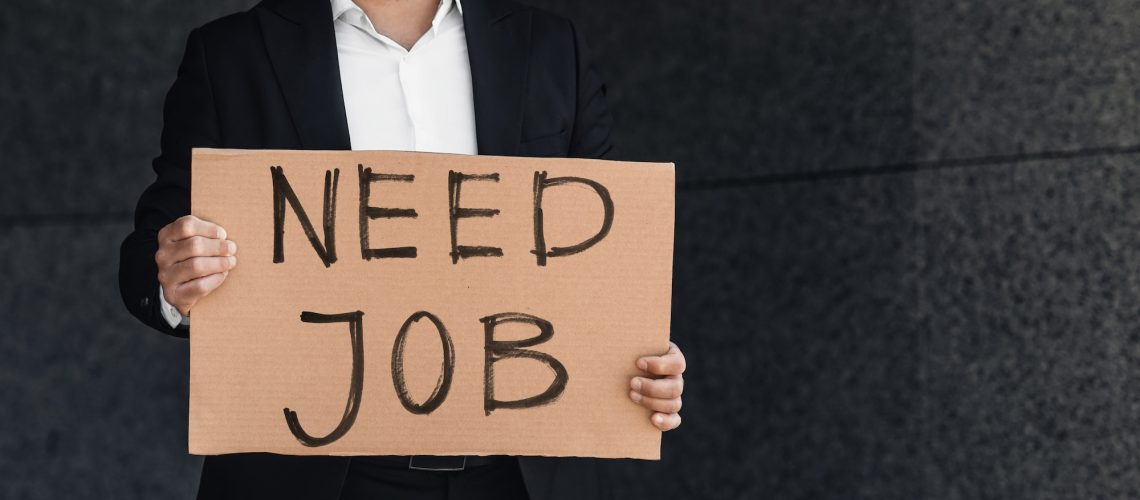 Despaired businessman lost work holding need job cardboard placard outside, standing near business