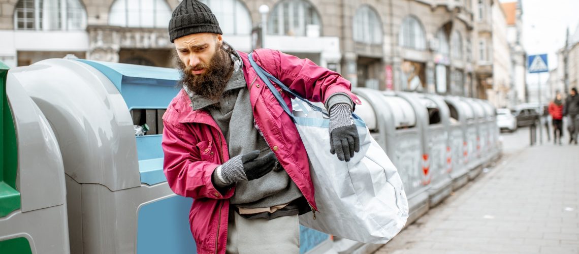 Homeless beggar near the trash containers in the city