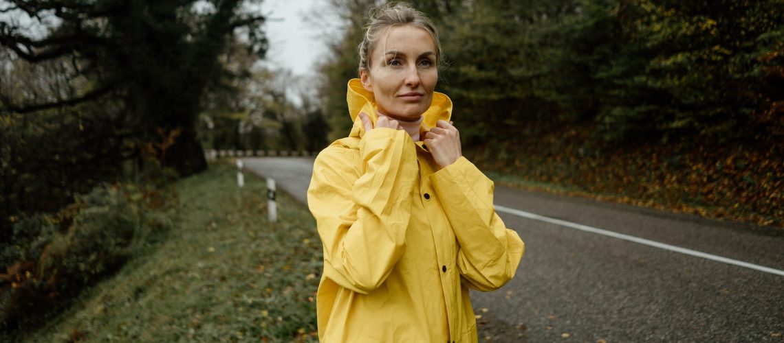 Pretty woman in yellow raincoat walking in rainy weather in the countryside