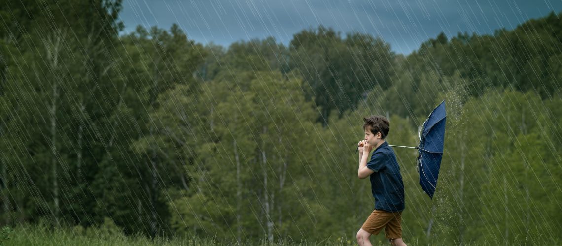 Teenager boy walking in the rain and strong wind. Weather