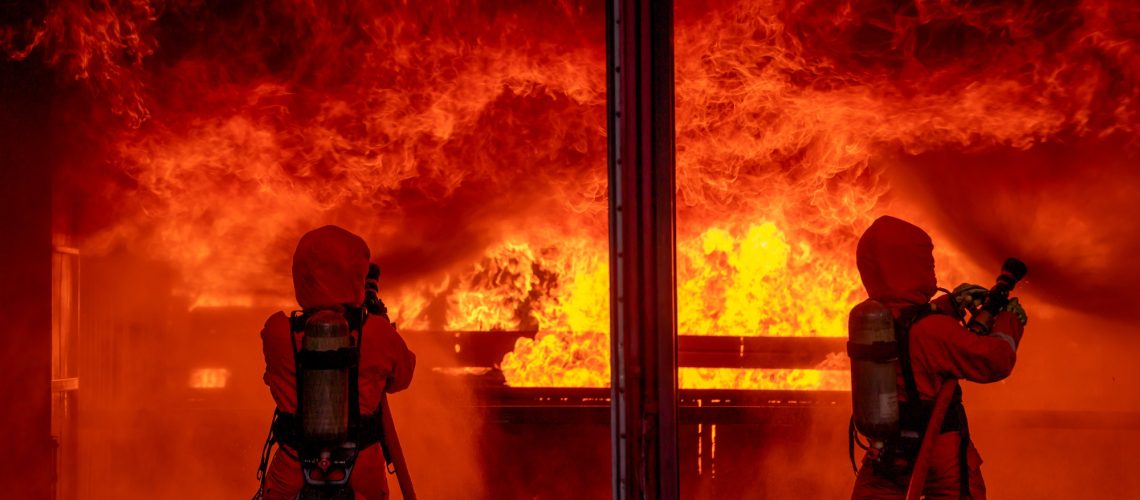 Two firefighters spray water by sprinkler to extinguish or get rid huge fire in room