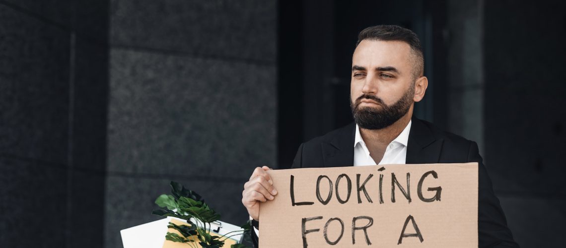 Unhappy unemployed man holding cardboard sign with Looking For a Job written text